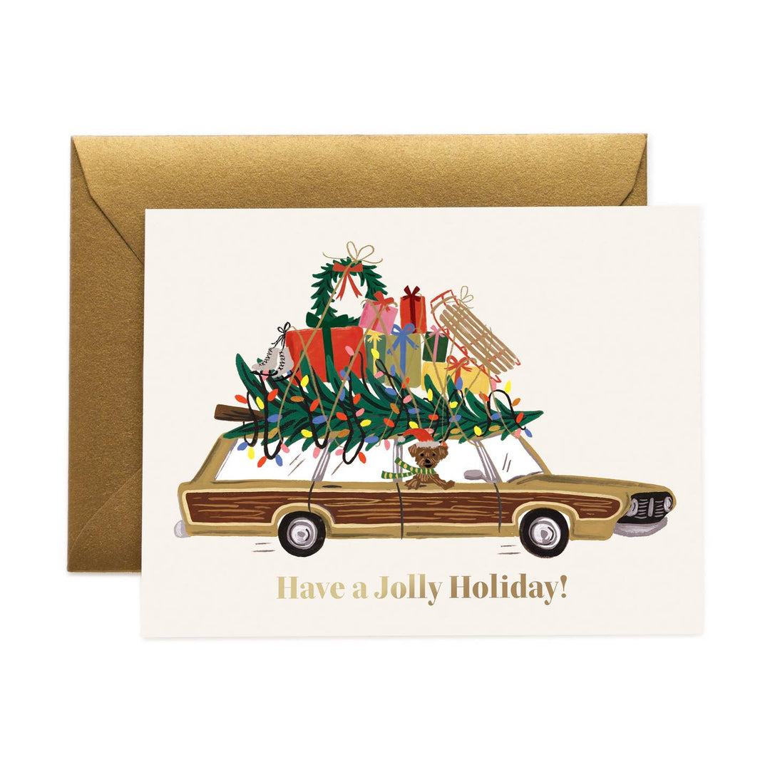 A holiday greeting card with a gold envelope, featuring an illustration of a vintage station wagon carrying a Christmas tree and wrapped gifts, with the text 'Have a Jolly Holiday!' printed below.