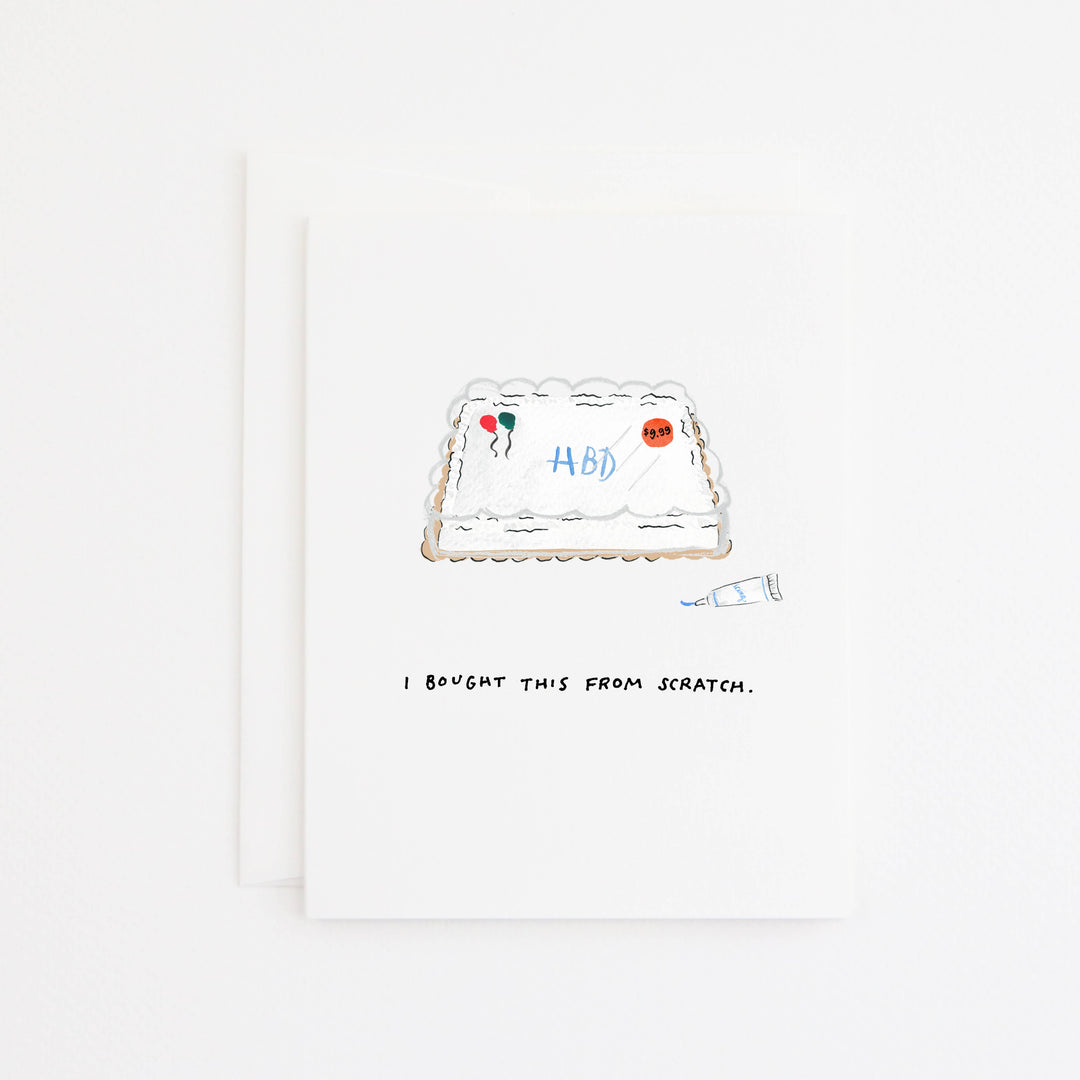A white greeting card with a hand-drawn illustration of a cake and the text 'I BOUGHT THIS FROM SCRATCH.' below it