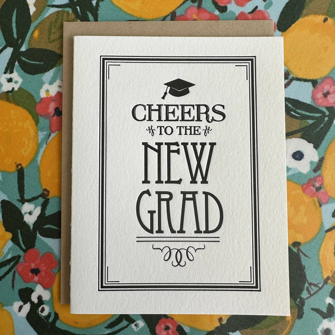 Black text with drawing of mortarboard above it and a formal stationery border on white cardstock