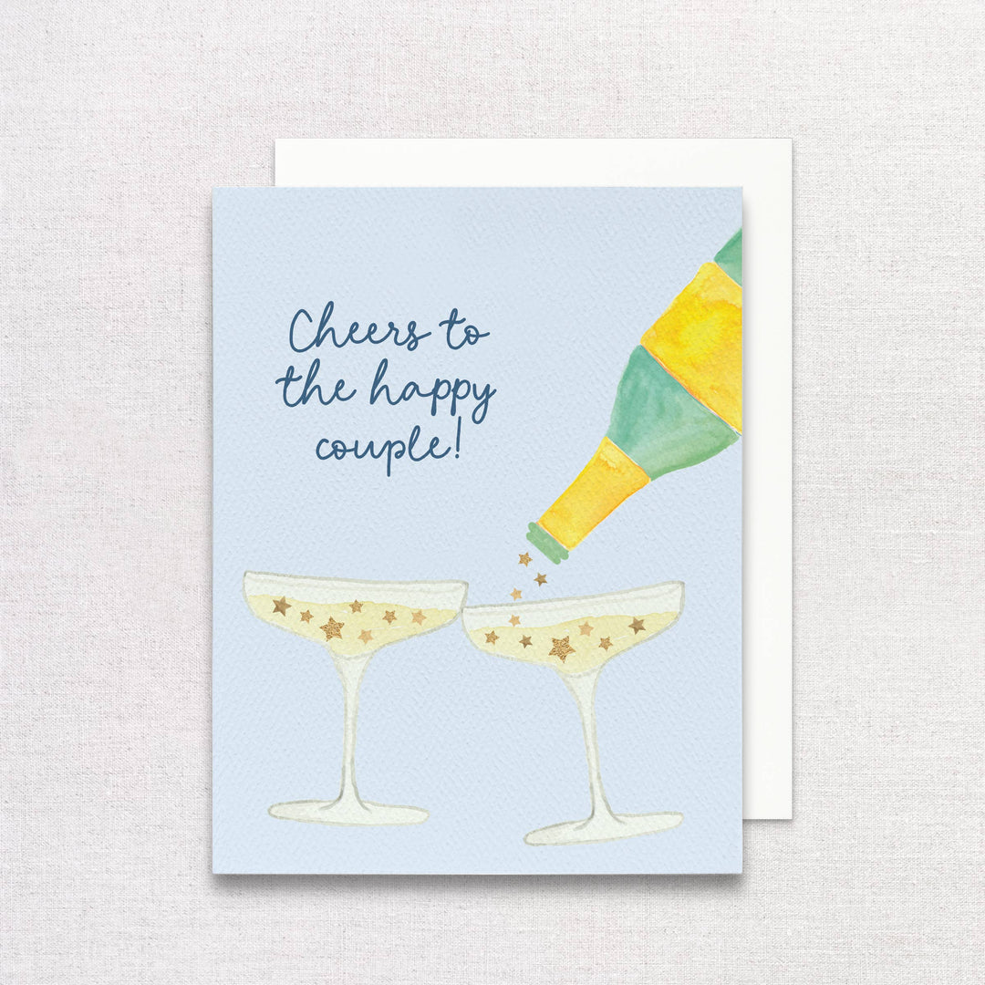 Front of card with bottle pouring stars into champagne flutes and 'cheers to the happy couple' text on a light blue background.