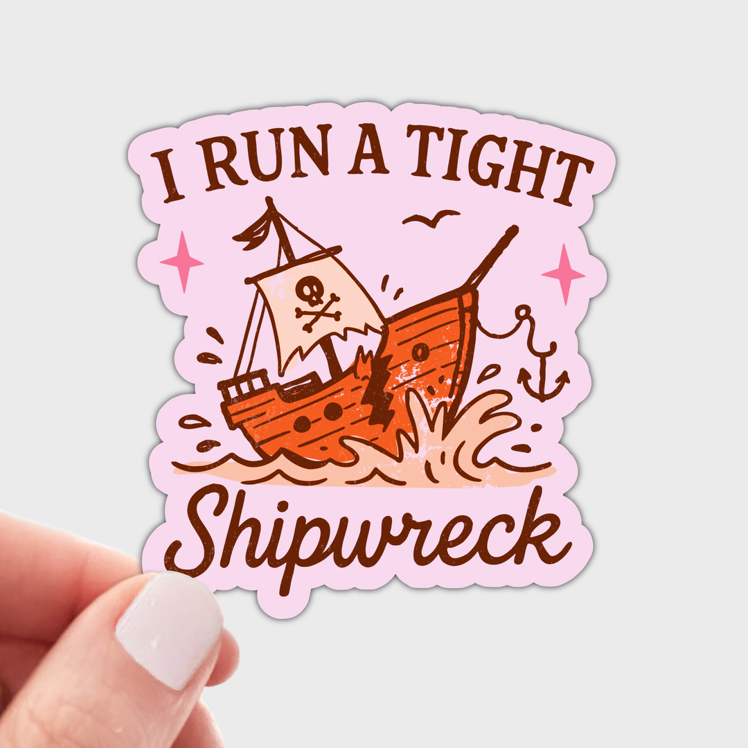 A die-cut sticker features a pink border and the text 'I RUN A TIGHT Shipwreck' in brown, surrounding a cartoon pirate ship sinking in orange and brown tones with small pink star accents.