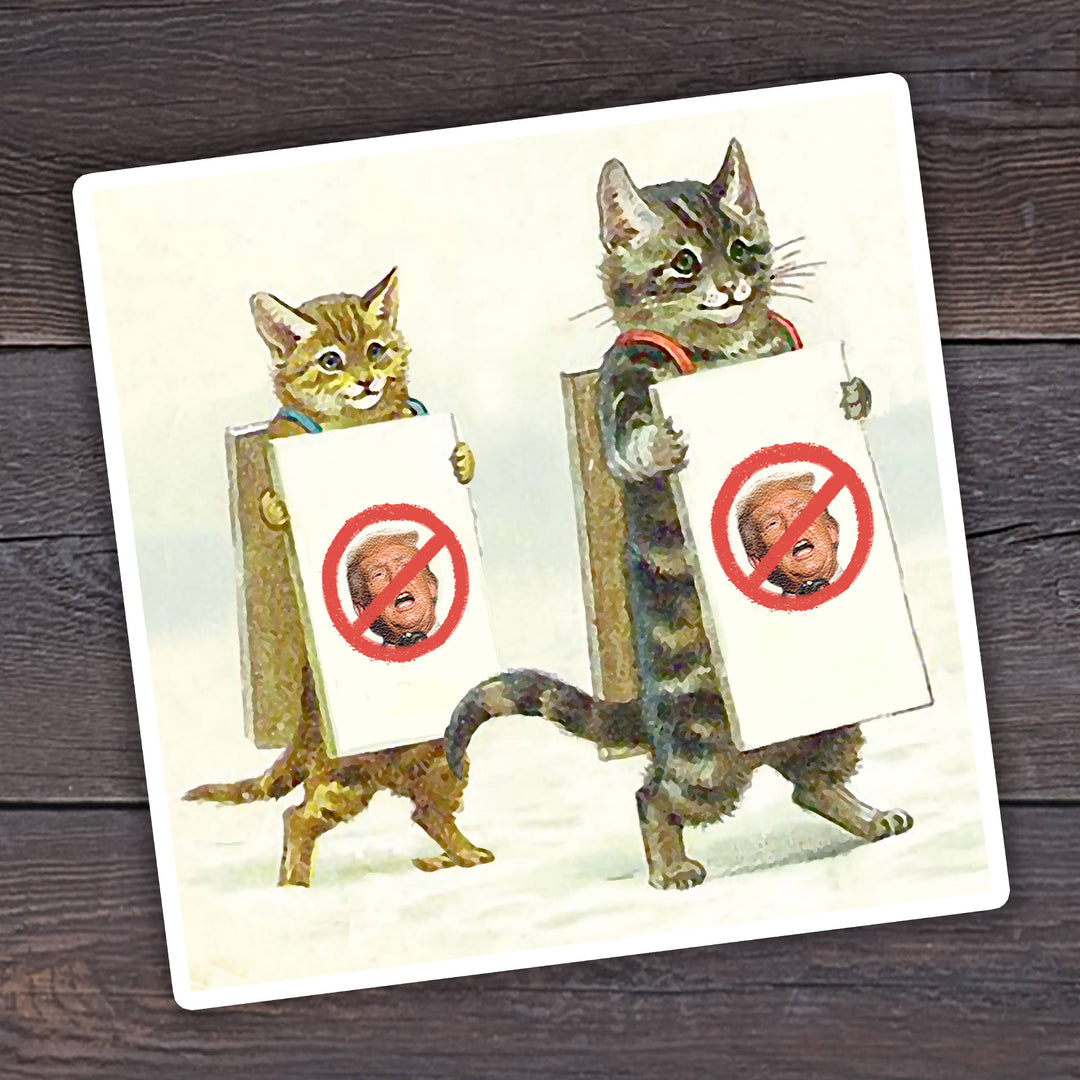 A die-cut vinyl sticker featuring two cats wearing sandwich boards with Donald Trump's face covered by the universal symbol for 'no'