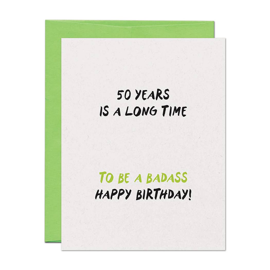 Birthday card with text '50 years is a long time to be a badass. Happy Birthday!' on a white background with green envelope behind it.