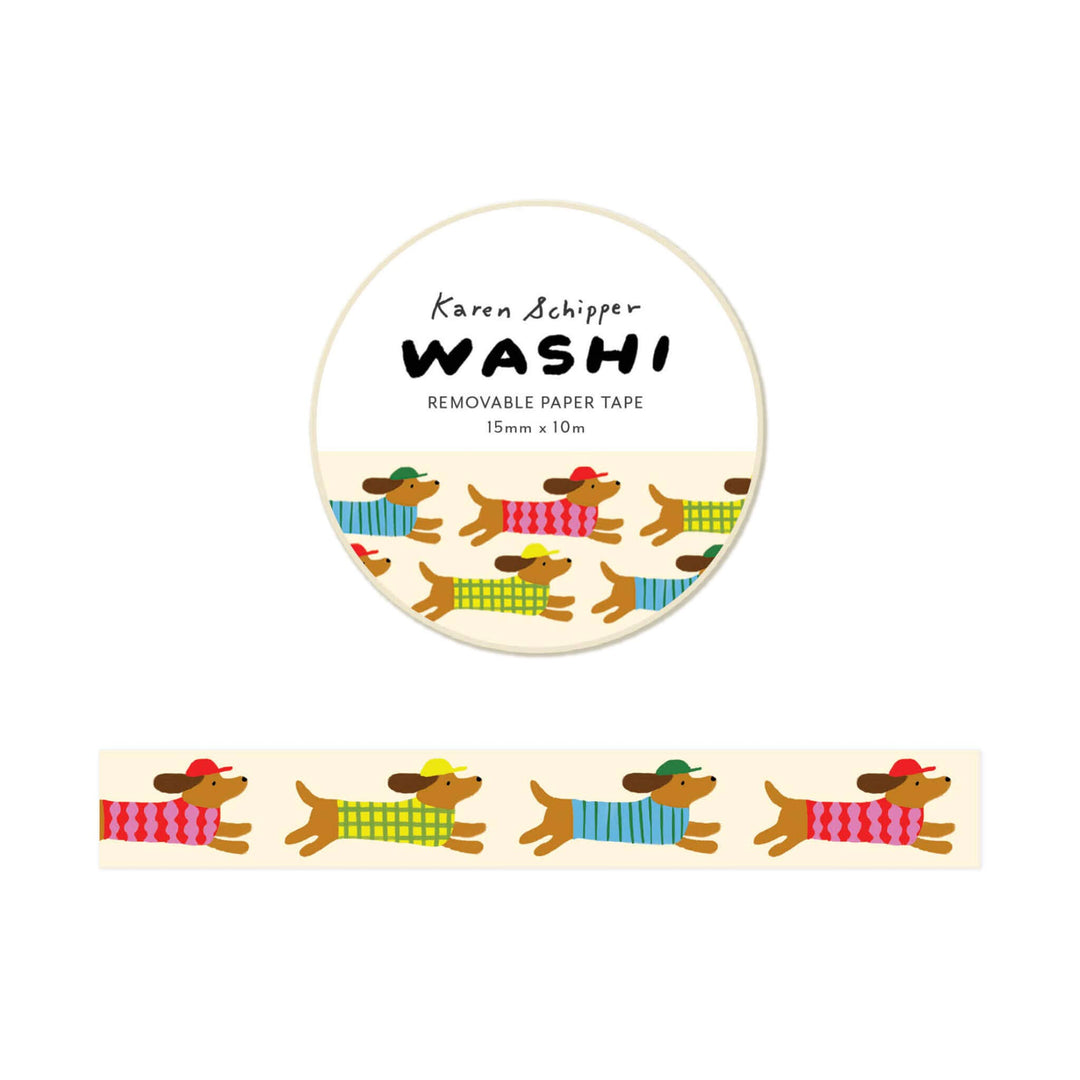 A roll of Karen Schipper Washi removable paper tape featuring a repeating pattern of dachshunds wearing colorful sweaters, shown with the circular label and a strip of the tape below.