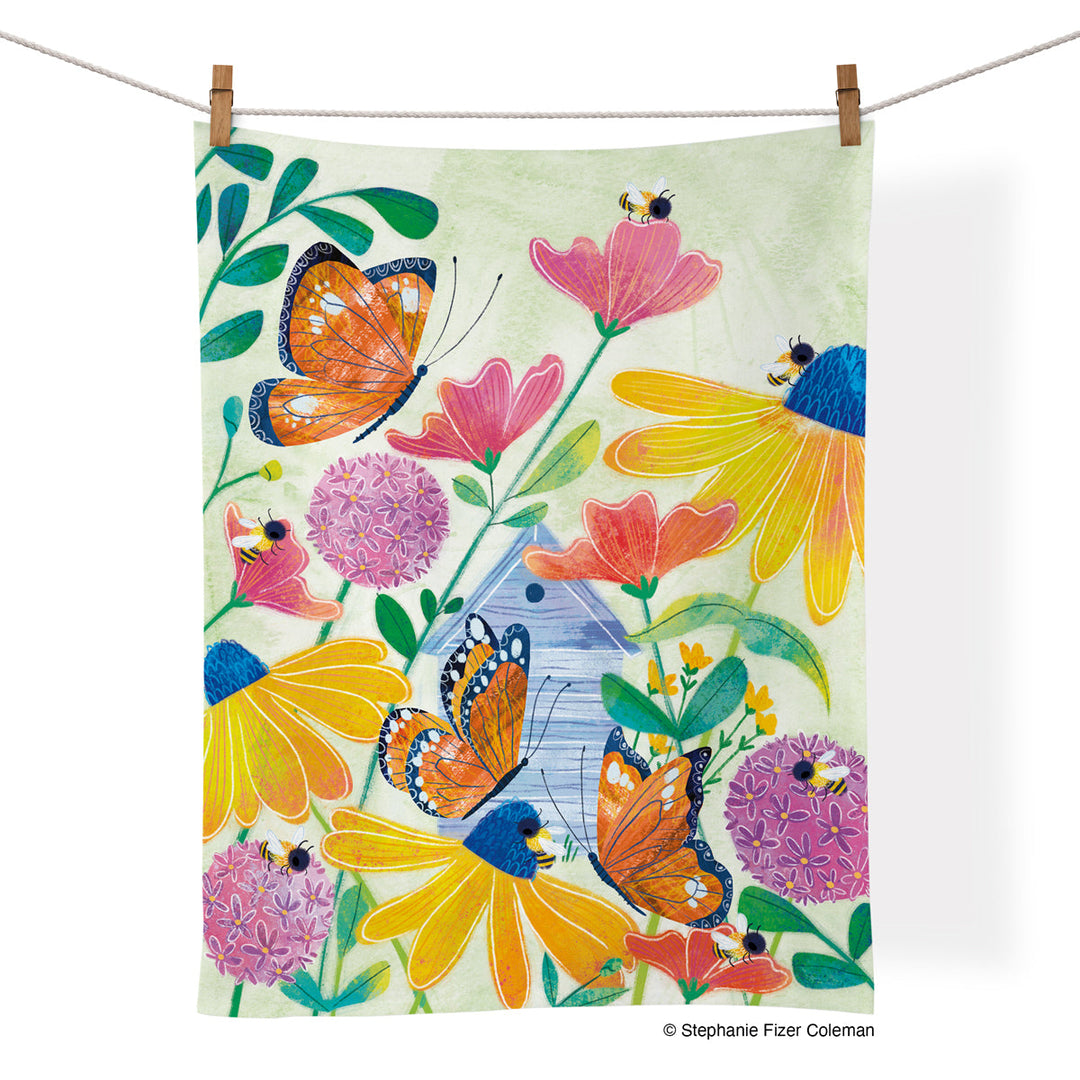 Cotton kitchen towel with colorful hand drawn butterflies and bees among flower tops. Predominant colors are pinks and yellows.