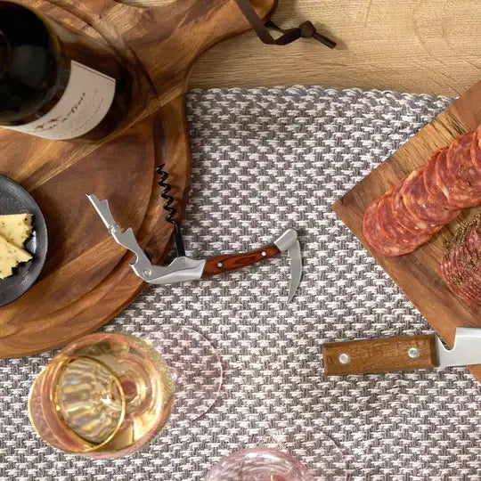 Waiter's corkscrew shown next to a cutting board with wine and cheese.