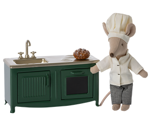 Mouse in chef's outfit next to kitchen island with sink and oven.