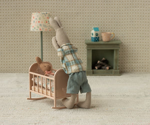 Mum mouse putting baby mouse to bed in the cradle in a room with a floor lamp and fireplace.
