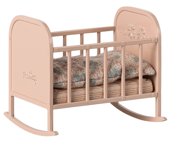 Pink metal cradle with striped mattress and patterned duvet.