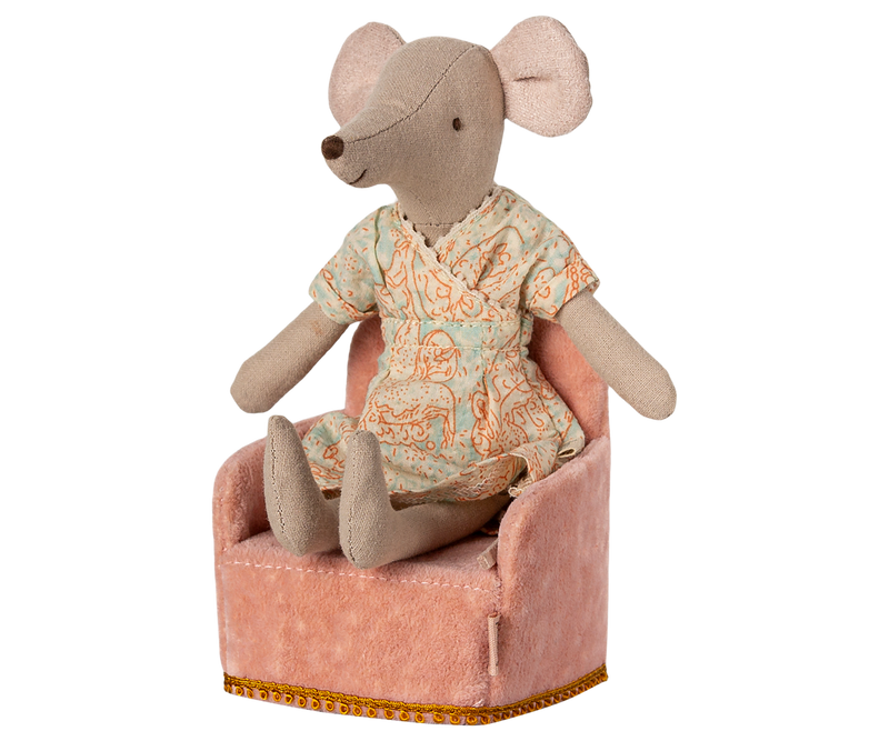 Mouse earing green and pink dress sitting in pink plush armchair.