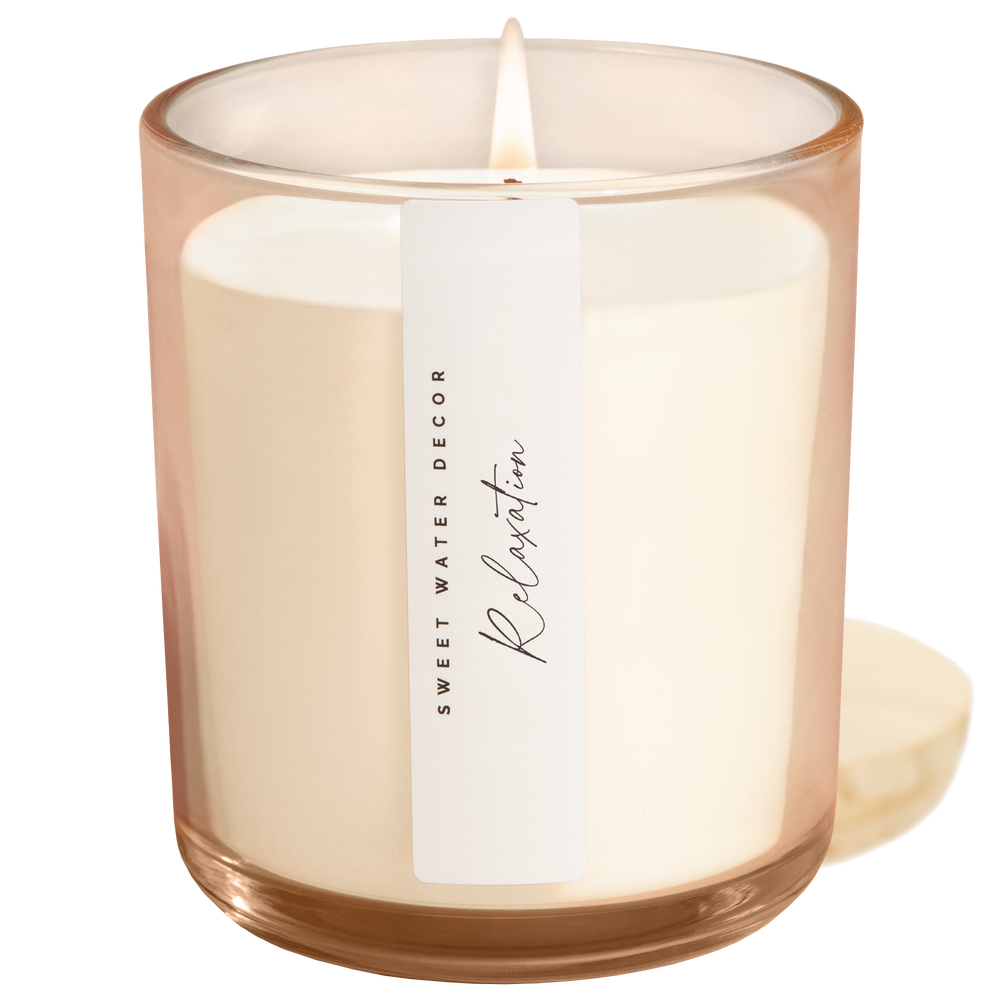 Lit candle in blush opaque container with vertical white label next to its wooden lid.