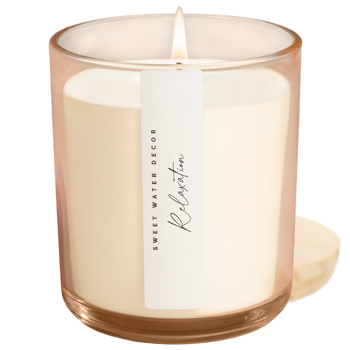 Lit candle in blush opaque container with vertical white label next to its wooden lid.