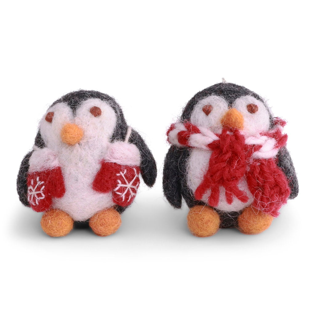 Two felt penguin ornaments on a white background, one wearing red mittens with white snowflakes and holding a small cup, and the other wearing a red and white scarf.