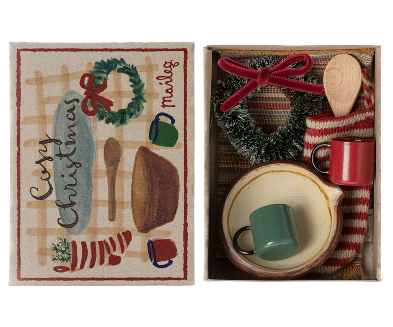 Red and white striped stocking in box bottom with a wreath, red and green mugs, and copper colored bowl with wooden spoon next to the box cover labeled "Cozy Christmas."