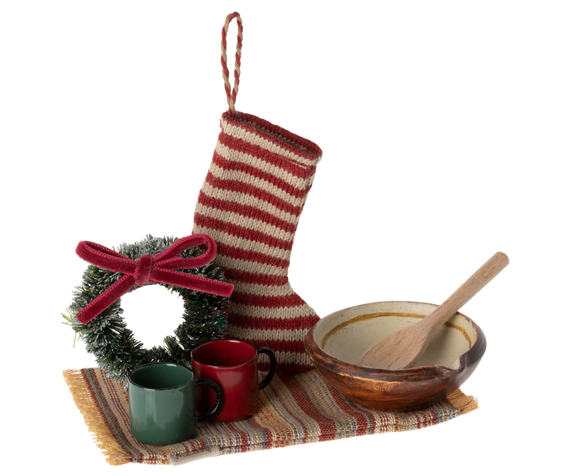 Red and white striped stocking surrounded by a wreath, red and green mugs, and copper colored bowl with wooden spoon.