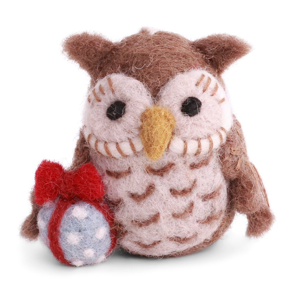 A brown and cream wool felt owl toy holding a small red bow and blue polka-dot gift bag, photographed on a clean white background.