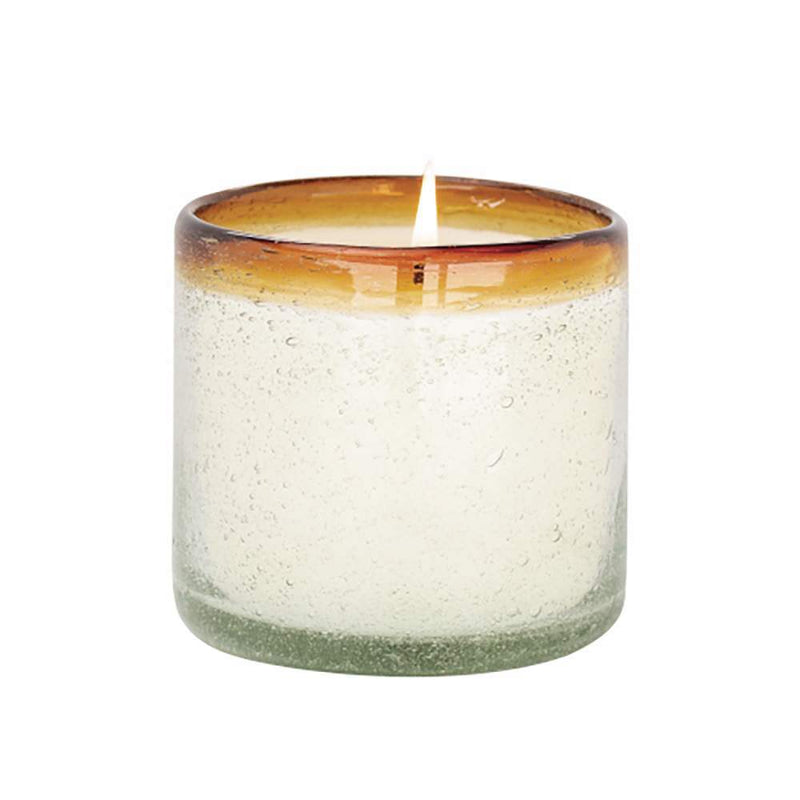 Lit candle in a handblown glass vessel with an orange rim.