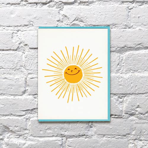 A smiling yellow sun with golden rays on white cardstock
