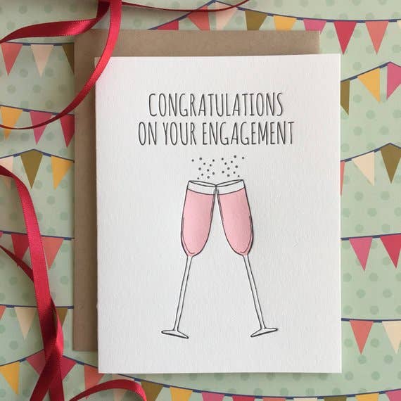 Two clinking long-stemmed glasses filled with pink champagne and black text on a white cardstock