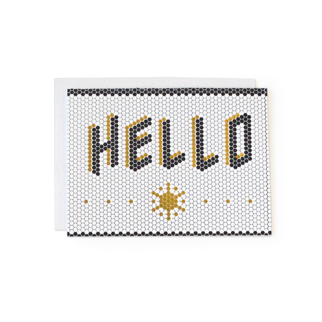 The word "Hello," in black with gold shadow, centered in a floor of honeycomb tiles.