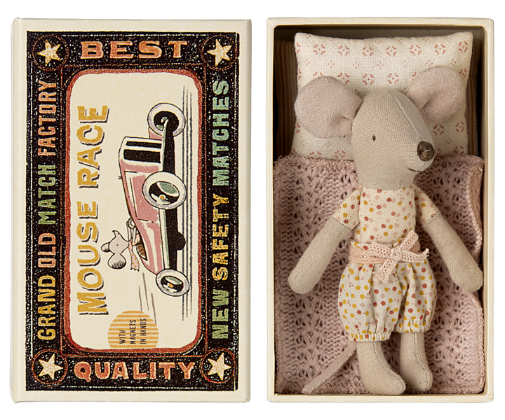 Mouse resting on a pink knitted blanket and pattered pillow, next to the lid of a vintage-style matchbox labeled 'Mouse Race.'