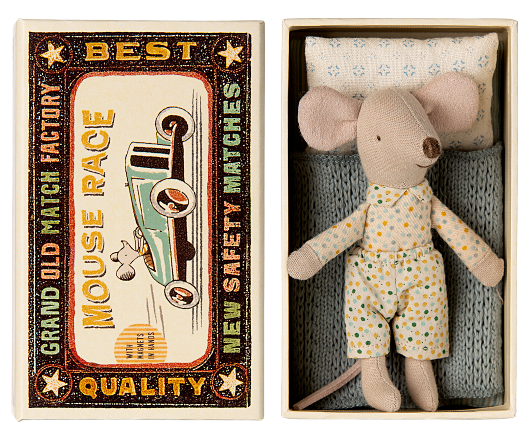 Mouse resting on a blue knitted blanket and pattered pillow, next to the lid of a vintage-style matchbox labeled 'Mouse Race.'