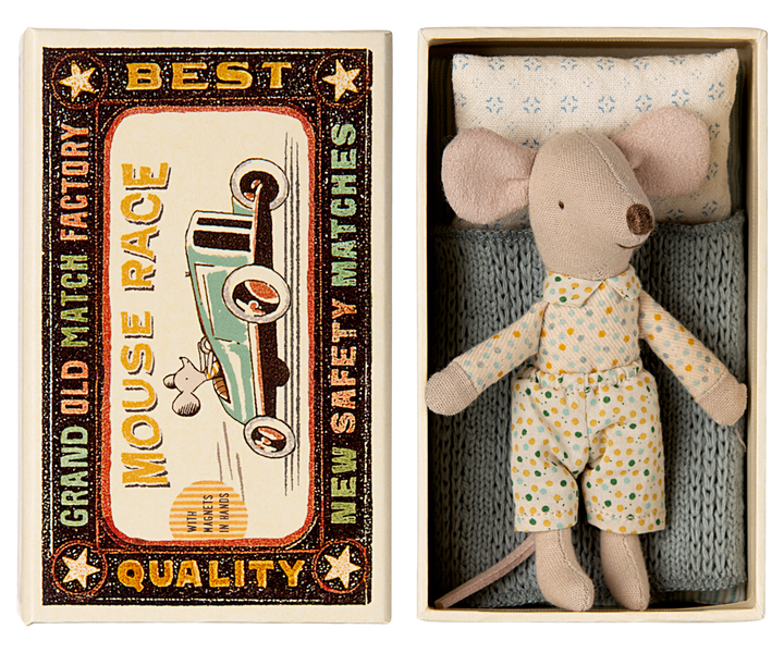 Mouse resting on a blue knitted blanket and pattered pillow, next to the lid of a vintage-style matchbox labeled 'Mouse Race.'