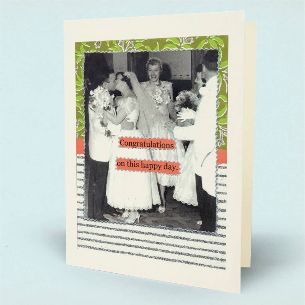 A  congratulations card shown standing upright. The card has an off-white border with a central black-and-white wedding photo framed by green and orange decorative borders, plus orange text reading 'Congratulations on this happy day.'