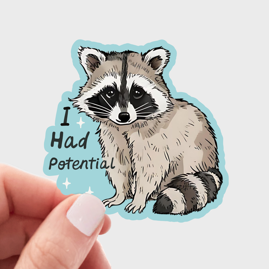A hand holds a die-cut sticker featuring an illustrated raccoon with the text 'I Had Potential' on a light blue background.