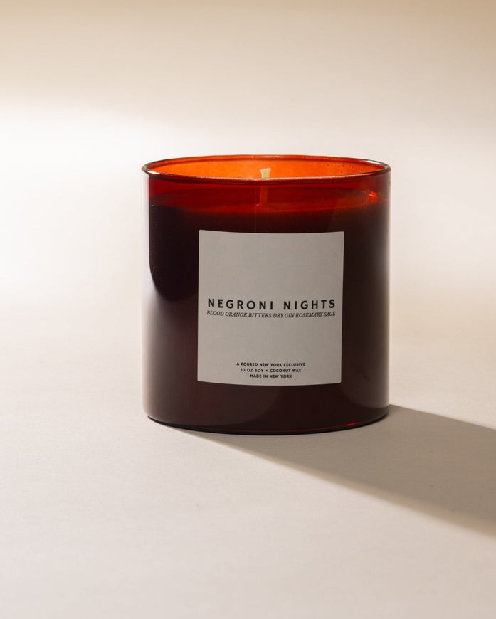An amber glass jar candle with a white label reading 'NEGRONI NIGHTS.'