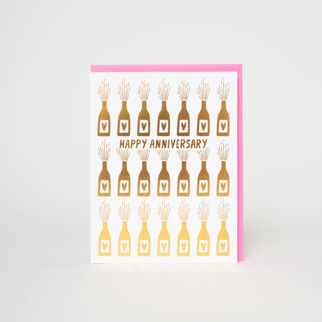 Three rows of gold foil champagne bottles with a heart label on white card. "Happy Anniversary" in all caps under the first row.