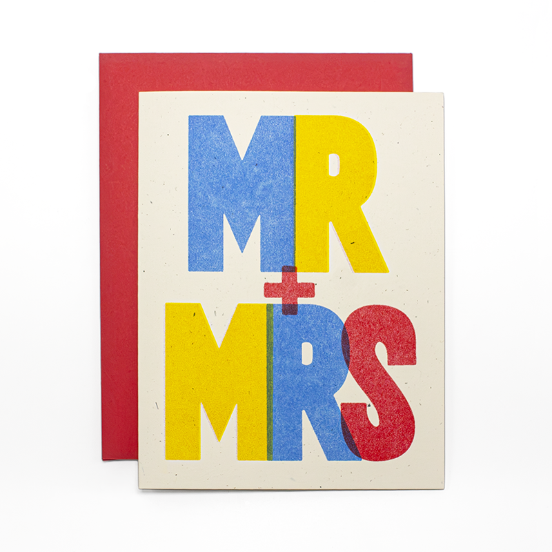 A greeting card with a cream textured background and bold multicolor lettering reading “MR + MRS” in blue, yellow, and red, shown with a red envelope behind it.