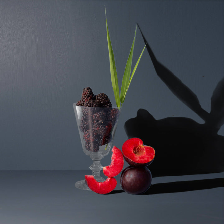 Glass filled with blackberries and a green leaf next to red grapes.