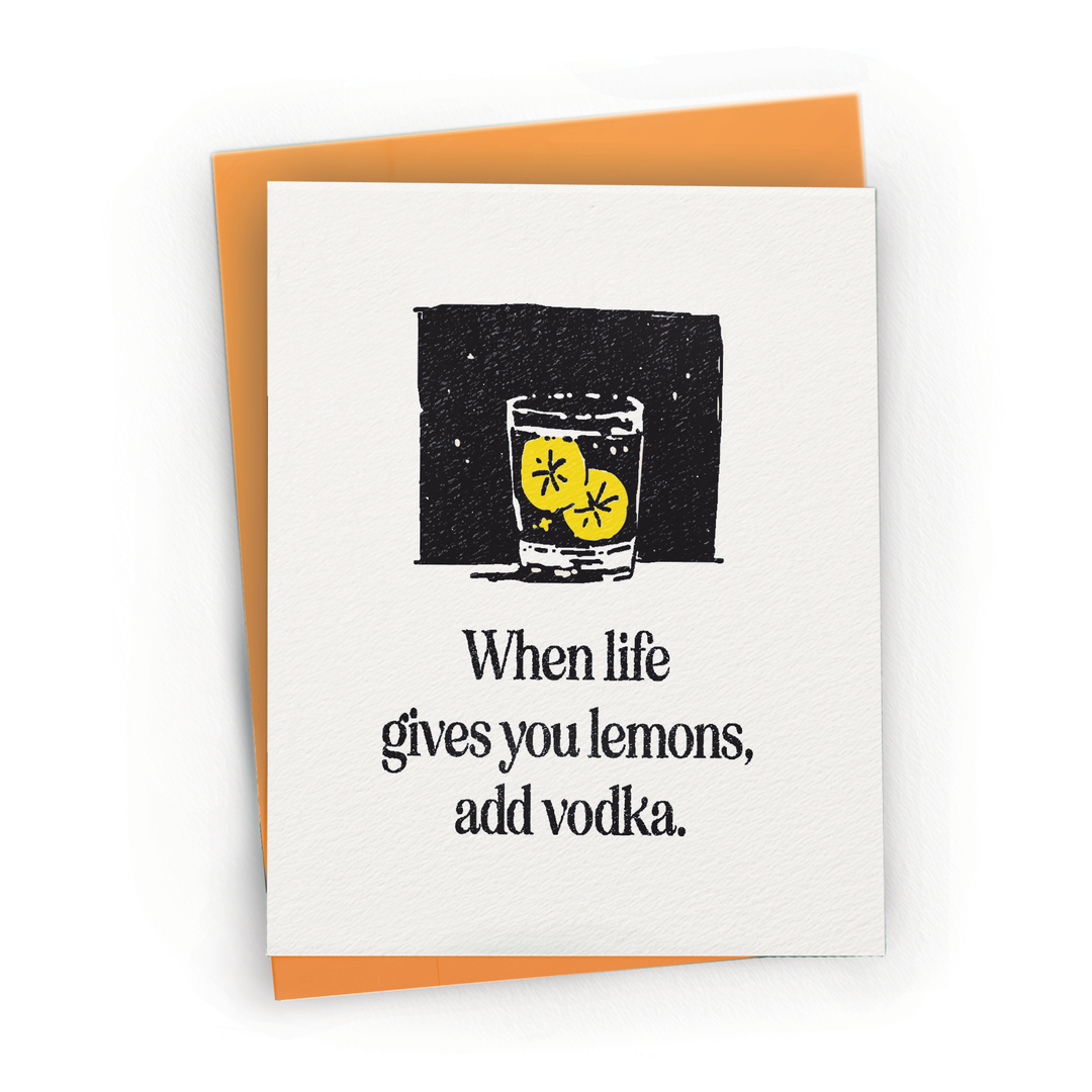 A white greeting card with a black-and-yellow illustration of a glass with lemons and the text 'When life gives you lemons, add vodka.' layered over an orange envelope.
