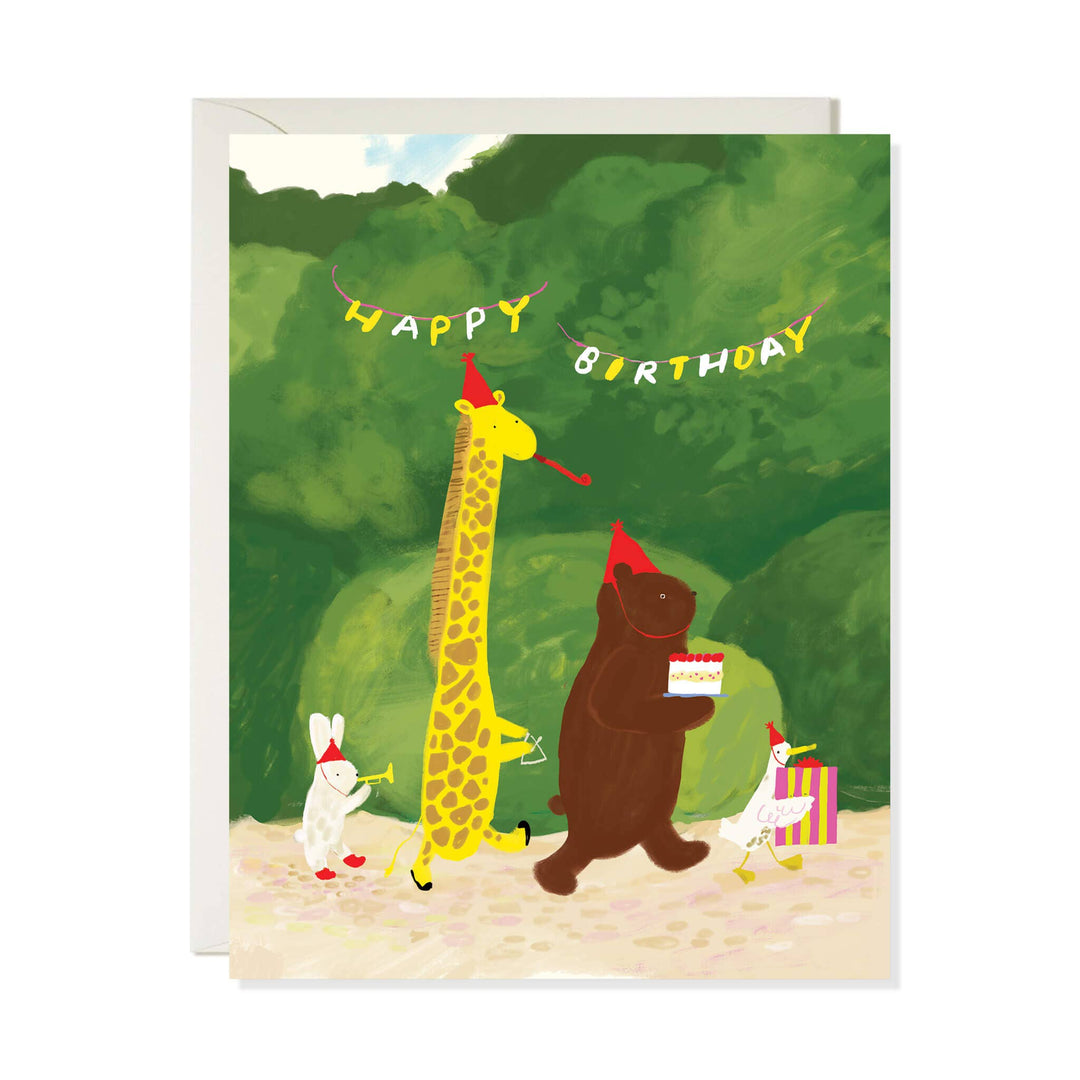 A birthday greeting card with a white envelope behind it, featuring a whimsical illustration of animals celebrating in a forest: a tall giraffe, a bear, a rabbit, and a bird with a striped gift box under a 'Happy Birthday' banner.