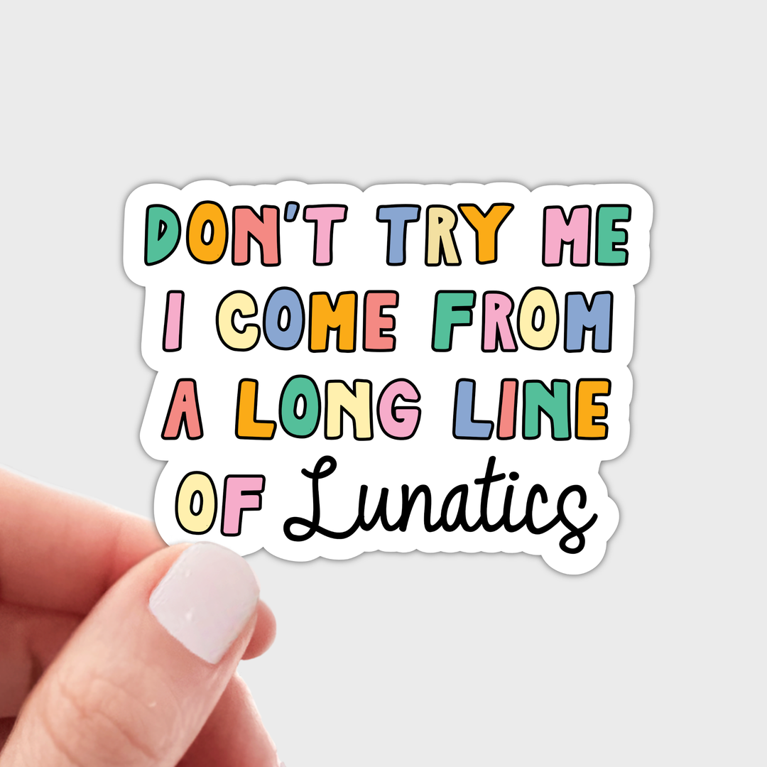A die-cut sticker held by a hand a. The sticker features the text 'DON'T TRY ME I COME FROM A LONG LINE OF Lunatics' in pastel-colored bubble letters with black outlines.