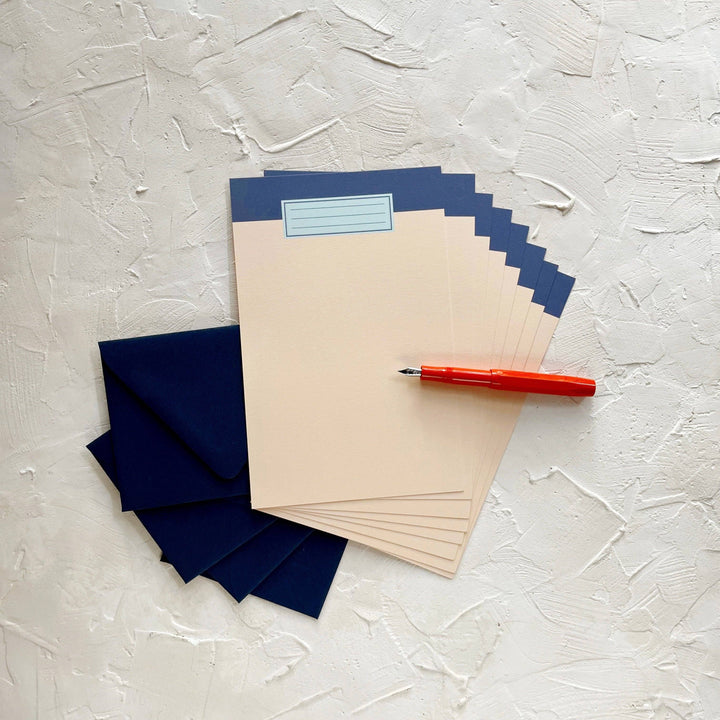 Eight sheets of peach paper fanned on top of navy envelopes. Each sheet has a navy blue band at the top and the drawing of a label reminiscent of the cover of essay books.  