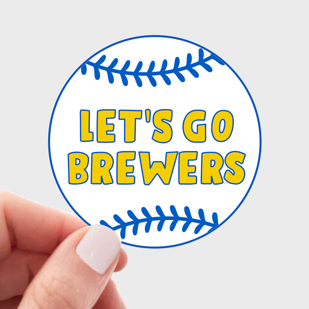 A hand holds a round sticker designed like a baseball. The sticker features blue line art of baseball stitching on a white background, with the text 'LET'S GO BREWERS' in bold yellow letters outlined in blue.