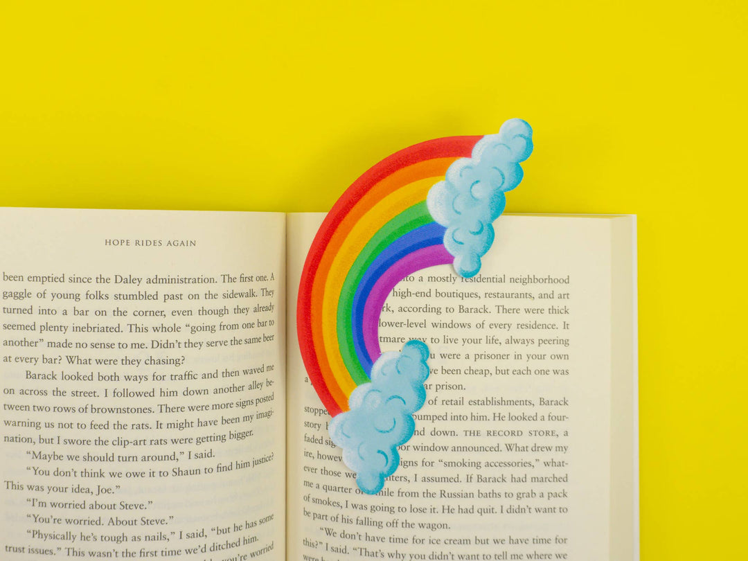 Open book with bookmark of a rainbow arc between two puffy clouds.
