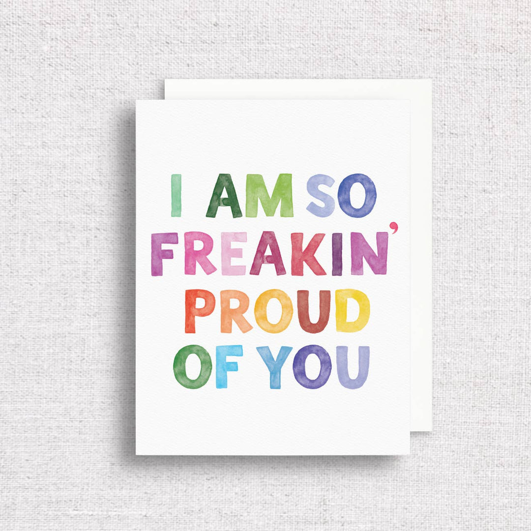 Front of card with text in uppercase letters and rainbow colors on a white background with a white envelope.