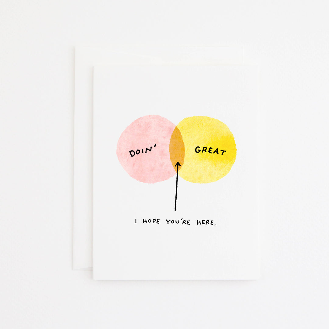 A white greeting card with a minimalist watercolor design featuring two overlapping circles, one pink and one yellow, with an arrow pointing to the shared orange-toned area. The words 'Doin'' and 'GREAT' appear inside the circles, with the handwritten text 'I HOPE YOU'RE HERE.' pointing to the intersection.