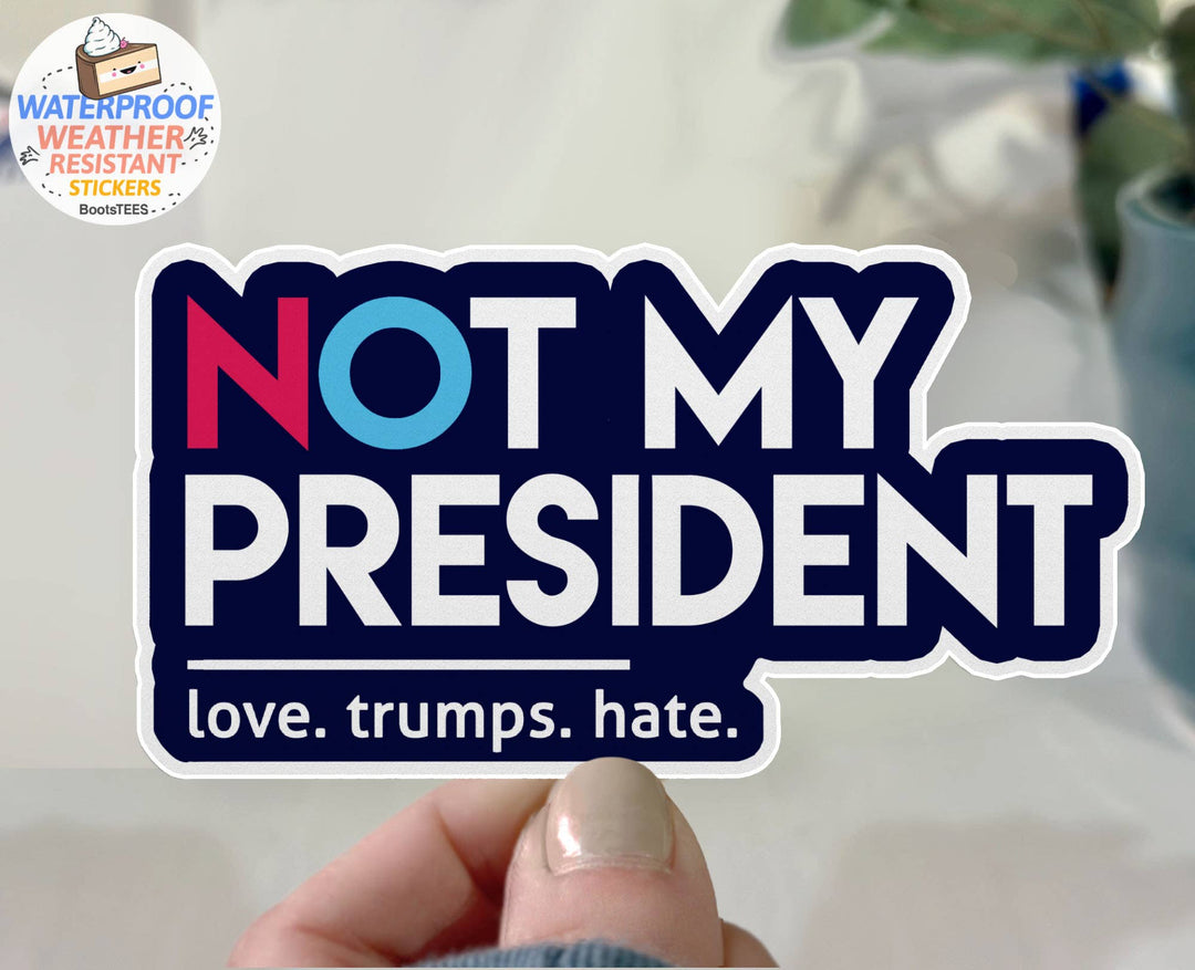 Die-cut vinyl sticker with the text 'NOT MY PRESIDENT' in bold white letters, with a red N and blue O, above the text 'love. trumps. hate.'
