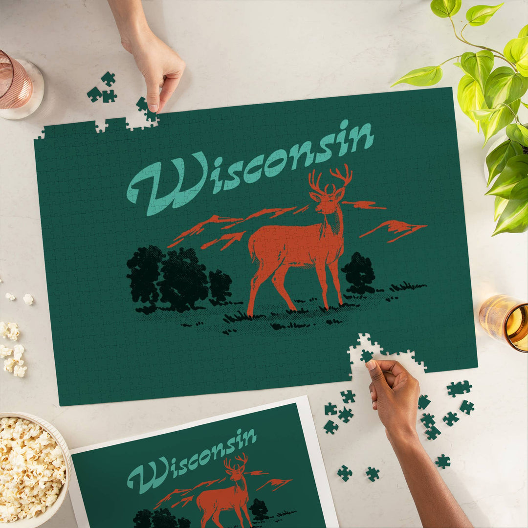 Hands of two people finishing the puzzle with 'Wisconsin' across the top and a drawing of a deer in a forest on a solid green background.