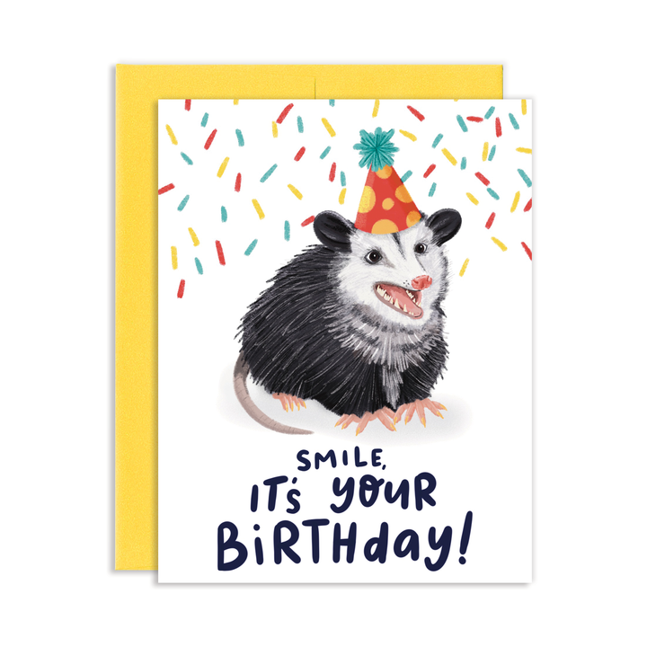Front of card with opossum wearing a party hat and surrounded by confetti above the text 'Smilem it's your birthday.'