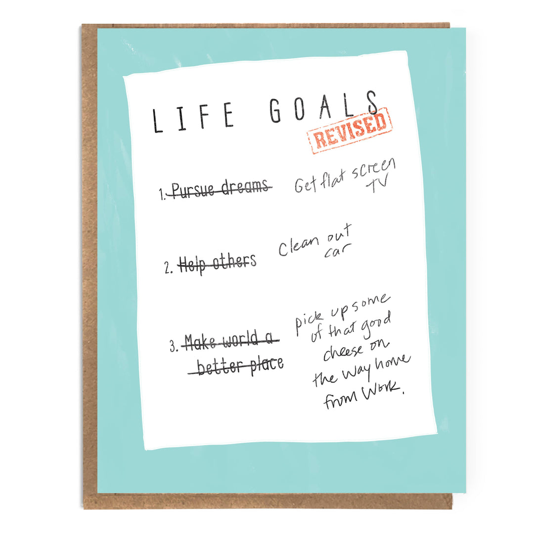 Hand-written text reading 'LIFE GOALS' and a red 'REVISED' stamp, set against a light aqua background with a brown kraft envelope behind it.  Each goal is crossed out and an updated version written next to it.