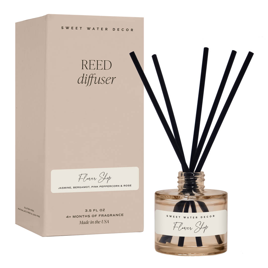 Five reeds in open short amber container with white label, next to gift box.