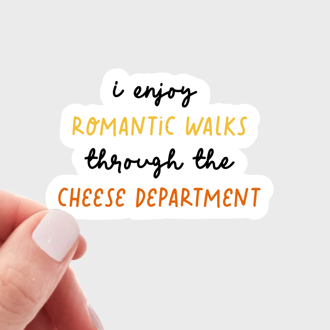 A hand with light pink manicured nails holds a die-cut sticker that reads 'i enjoy ROMANTIC WALKS through the CHEESE DEPARTMENT' in black, yellow, and orange lettering on a white background.