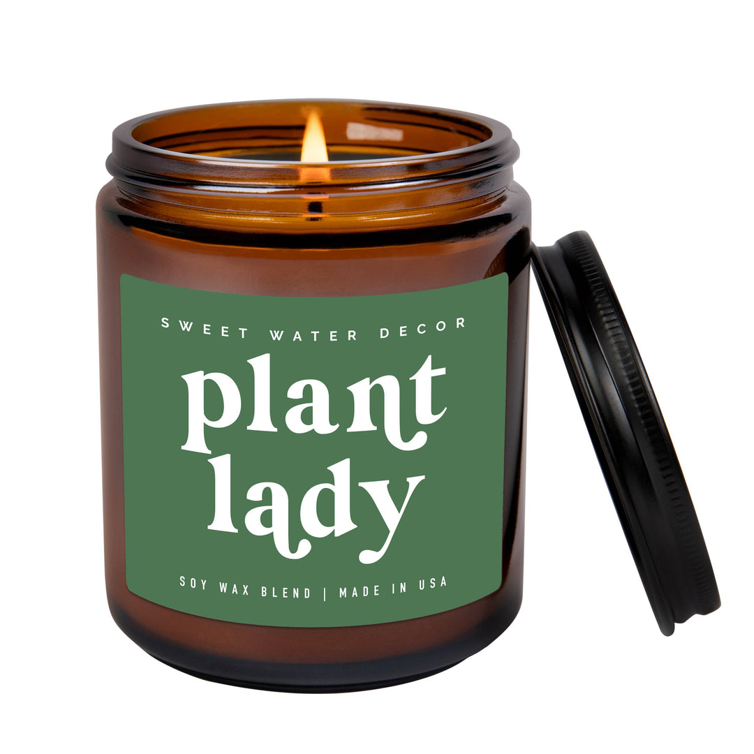 Scented soy candle in amber glass container with black metal lid. Green label says  Plant Lady