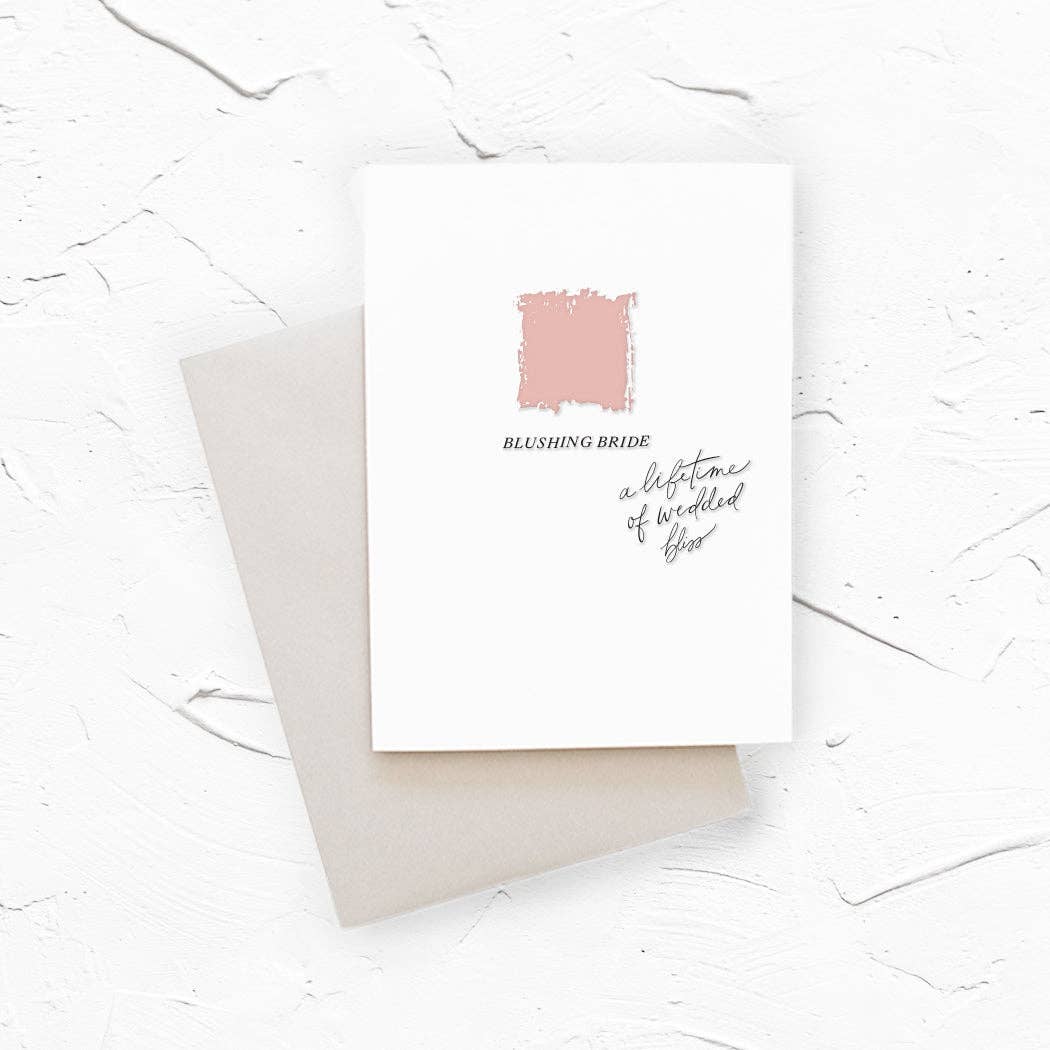 Cover of a card for a bride with a light pink paint stroke and the text 'BLUSHING BRIDE' and 'a lifetime of wedded bliss' in black, shown with a light gray envelope.