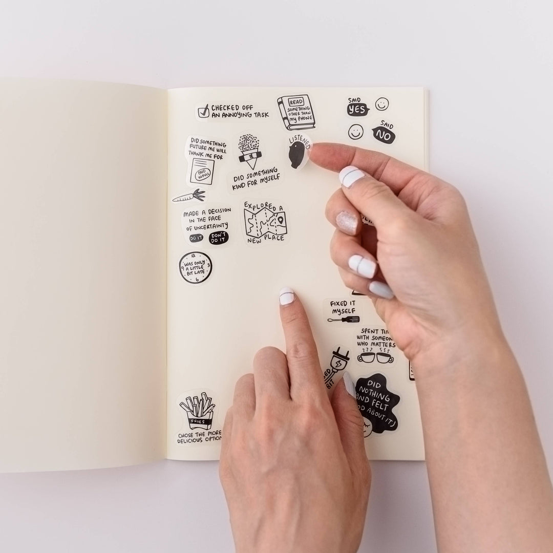Open notebook with hands of a person placing stickers on the page.